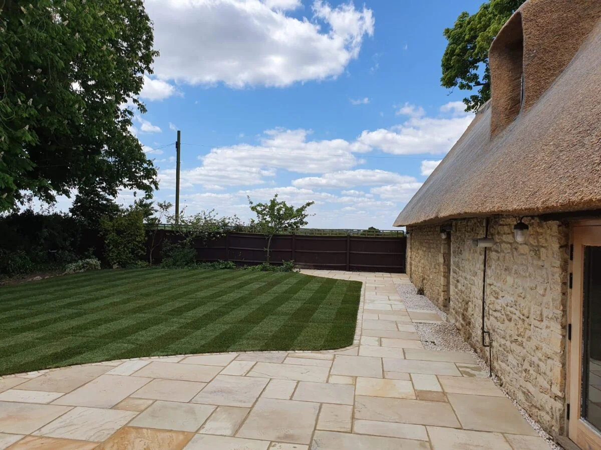 WV Landscapes' completed garden with sandstone patio, manicured lawn and thatched cottage